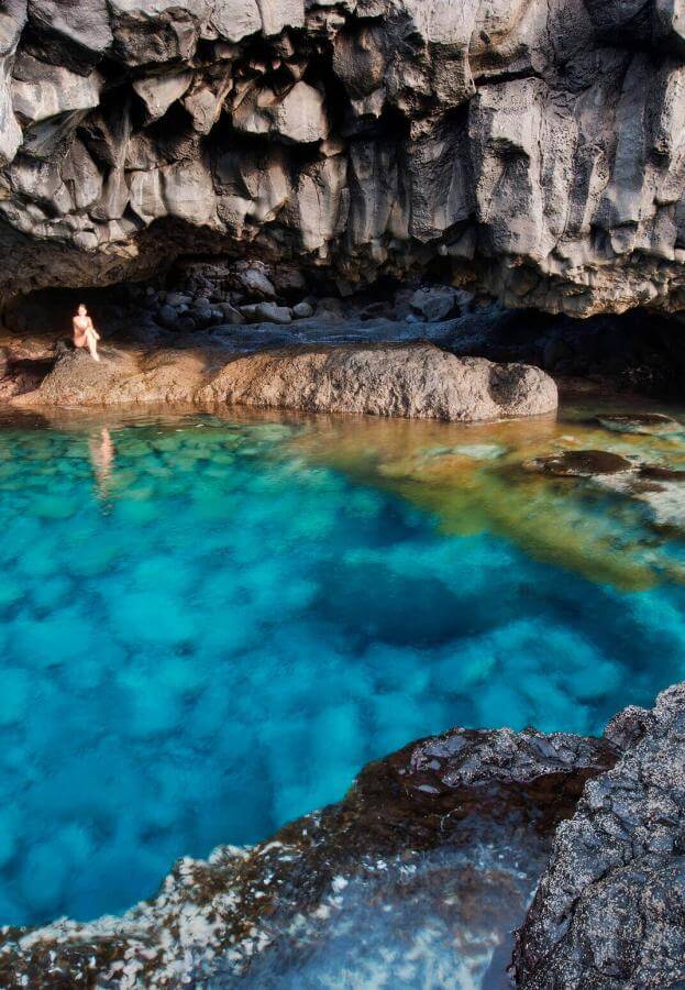 Charco Azul El Hierrolla, sinivetinen luonnonlampi tummien kivien ympäröimänä jyrkänteen alla.