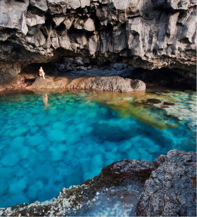 Charco Azul El Hierrolla, sinivetinen luonnonlampi tummien kivien ympäröimänä jyrkänteen alla.